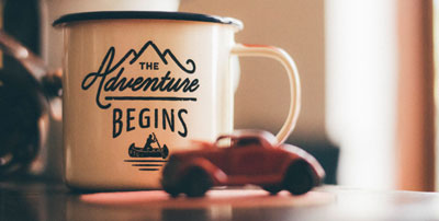 A cup of coffee that says "the adventure begins"